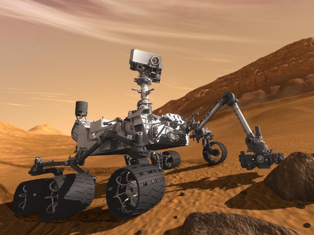 Un rover de Marte navegando por el terreno rocoso y rojizo de la superficie marciana sin conductor humano, guiado por cámaras y software a bordo