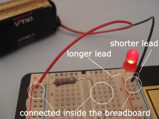 Paso 6: LED encendido en el circuito de la protoboard, con la pata larga (anodo) y la pata corta (catodo) senaladas donde se conectan a la resistencia y al riel negativo
