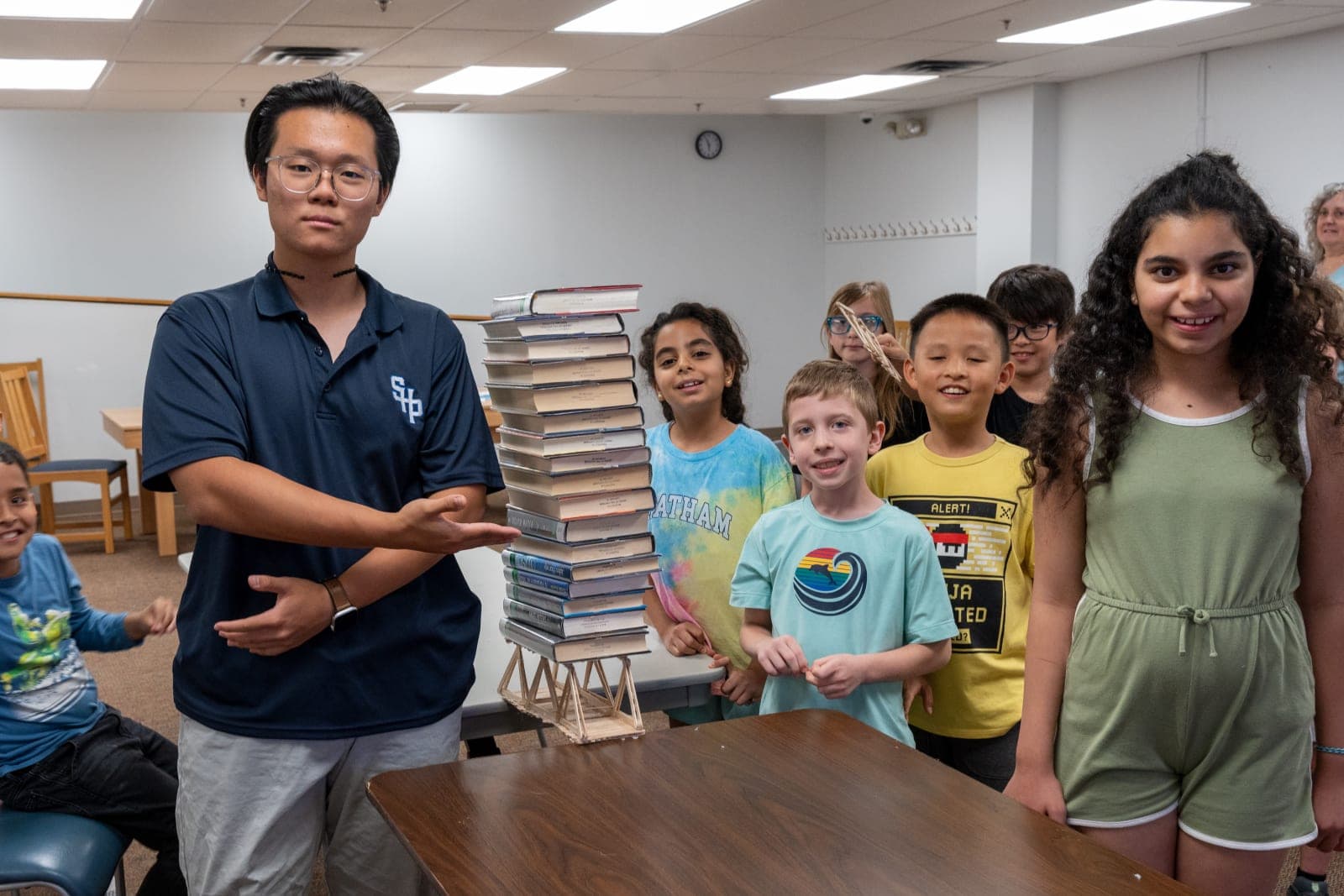 Mentor y estudiantes de Avanza STEM junto a un puente de palitos que sostiene una pila alta de libros