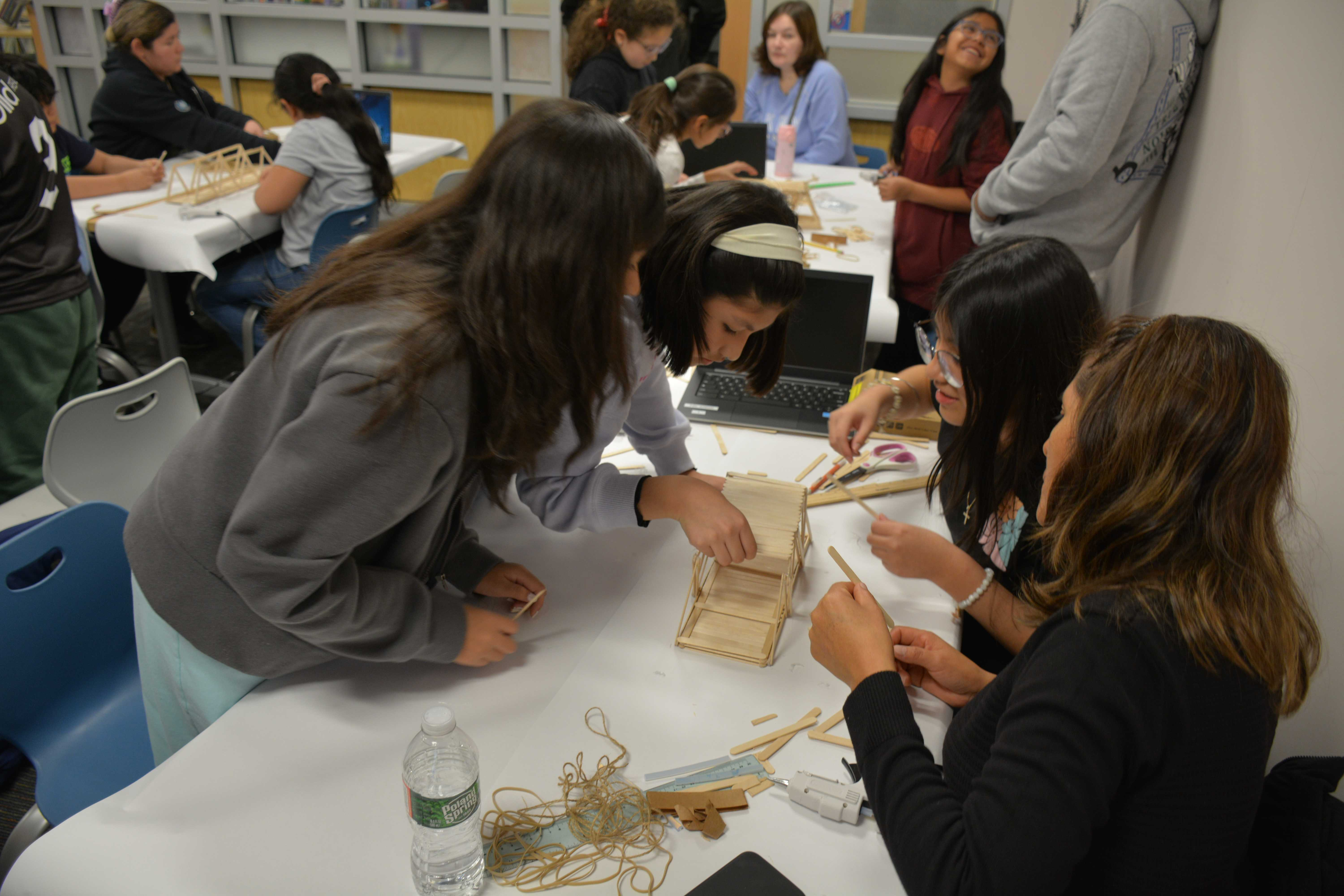 Young Hispanic youth collaborating on a popsicle stick engineering project at a workshop table